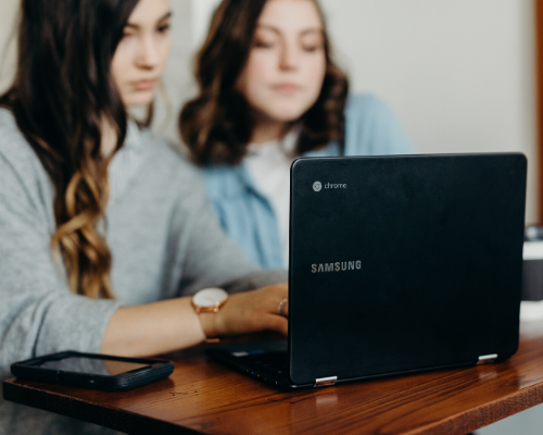 Zwei Frauen sitzen vor einem Laptop und sehen sich gemeinsam etwas an